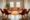 Empty therapy room features orange armchairs arranged in circle on round orange carpet. Natural light streams through windows. Plant sits in center of room. Suitable for group therapy sessions,